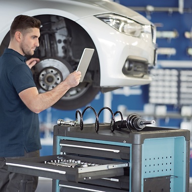 Un mécanicien vérifie un véhicule dans un atelier tout en regardant une tablette.